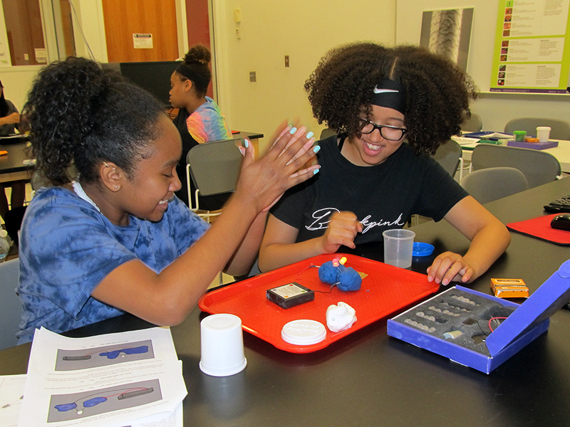 Two young girls participate in a science experiment during a school outreach program.