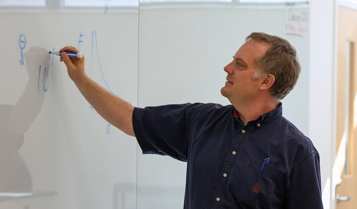 Jeremy Armstrong writing equations on a white board in a classroom.